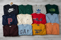 Flat lay of 10 assorted branded sweatshirts spread out on a wooden surface